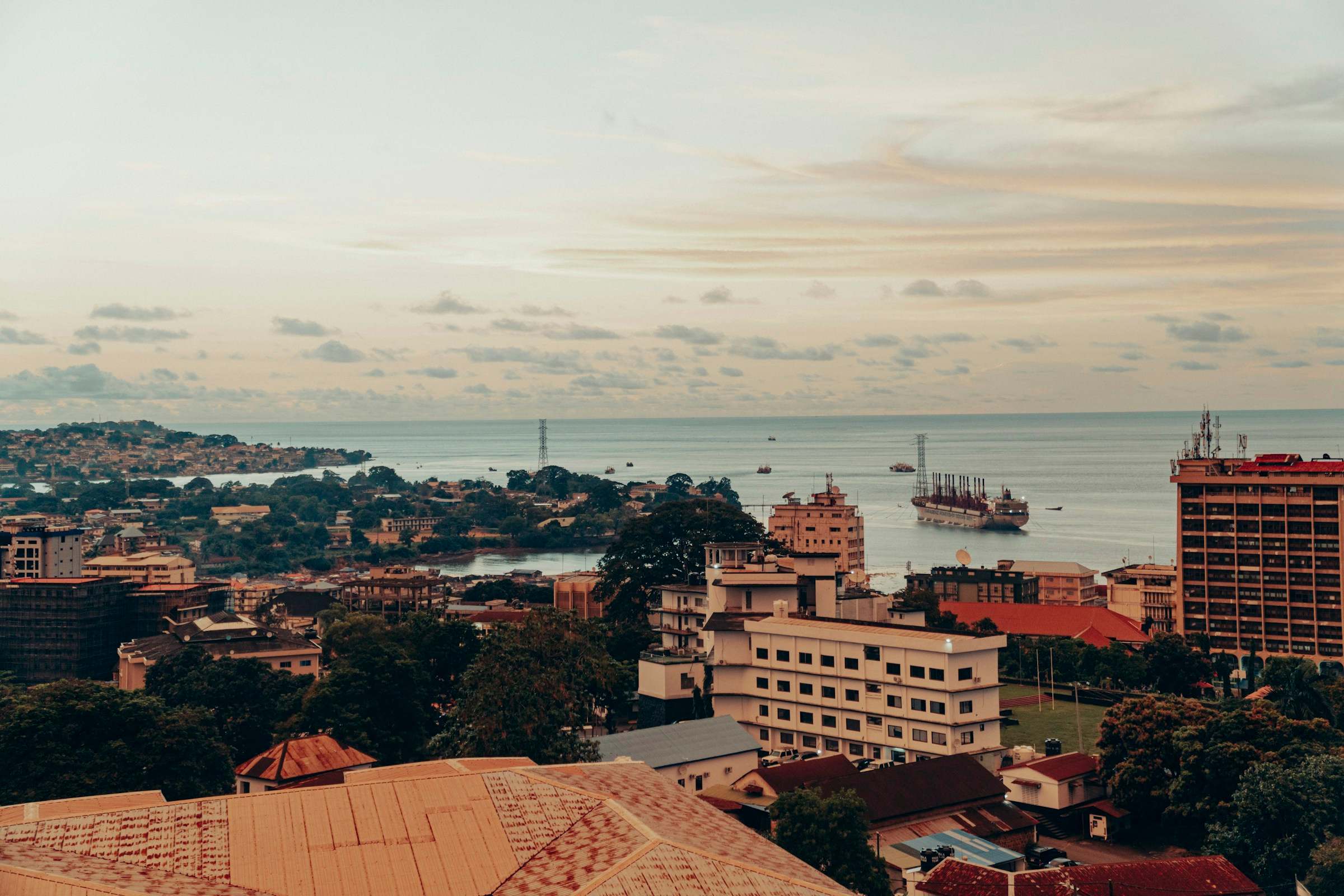 Rooftops of central Freetown running down to the harbour at dusk, with ships at anchor in the bay