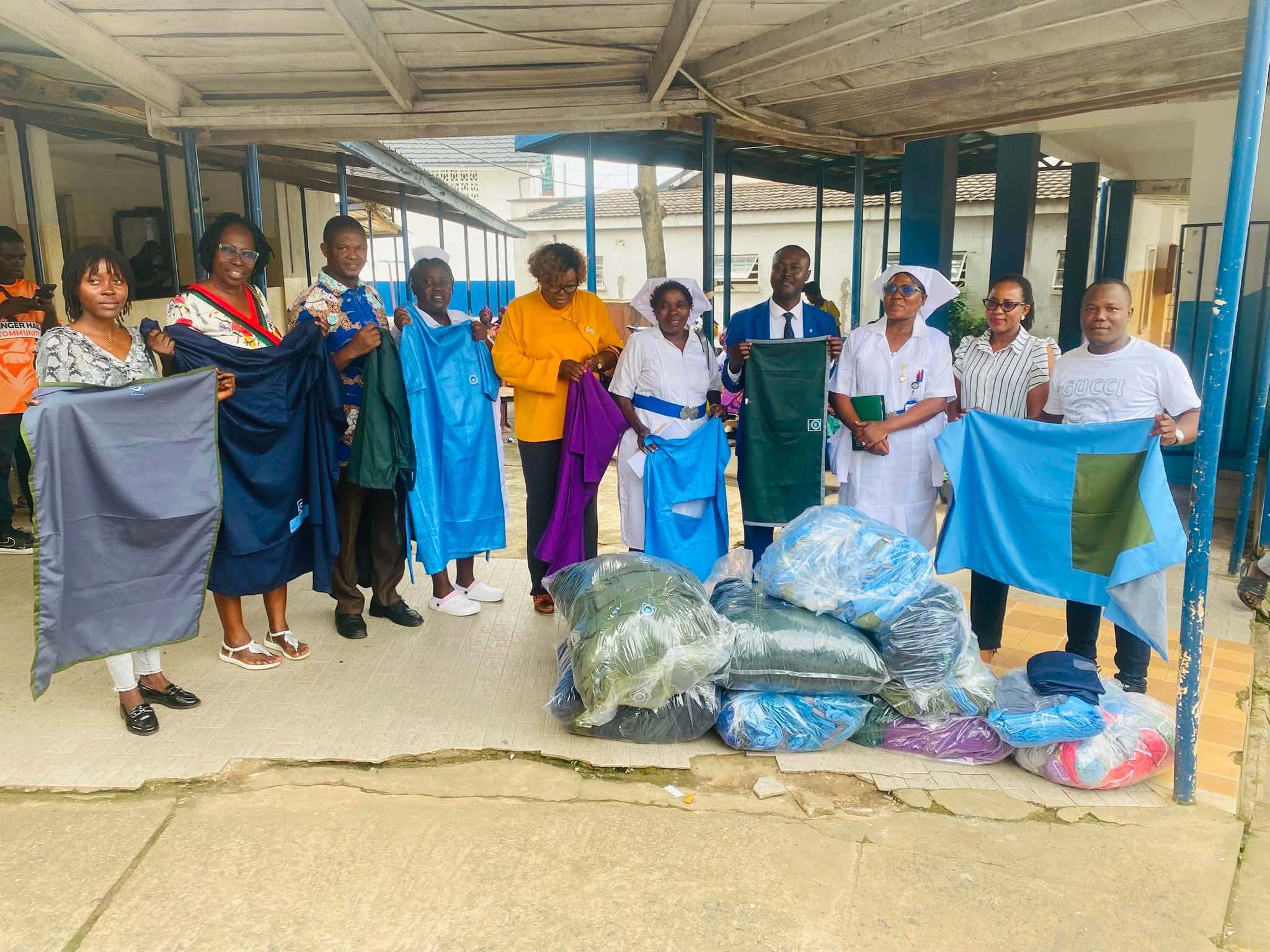 Health workers and programme staff holding up theatre linen at the handover for the National IPC Programme: gowns, sheets and drapes, with packed bags of linen in front