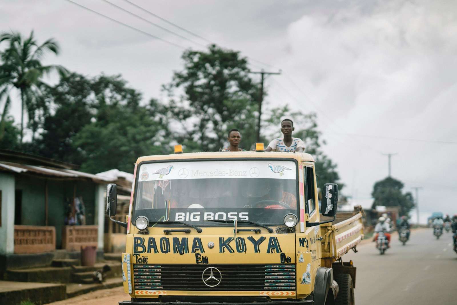 A yellow cargo truck painted with the words Baoma Koya on a road in Sierra Leone